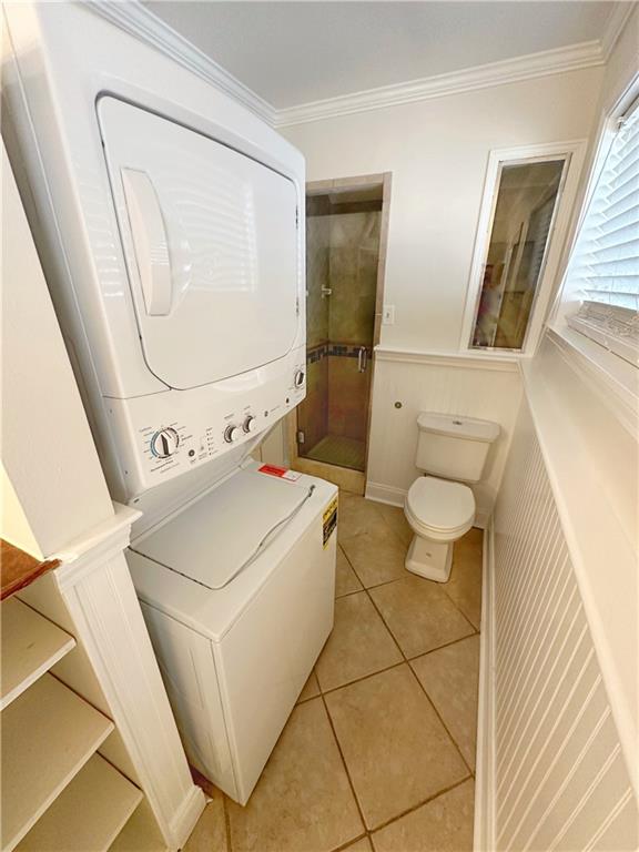 clothes washing area featuring ornamental molding, light tile patterned floors, and stacked washer / drying machine