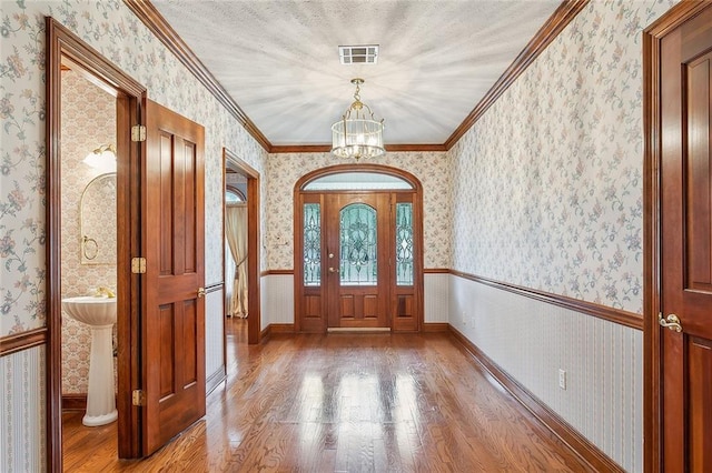 foyer entrance featuring crown molding, wood-type flooring, a textured ceiling, and an inviting chandelier