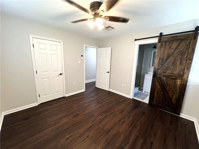 unfurnished bedroom with ceiling fan, ensuite bathroom, a barn door, and wood-type flooring