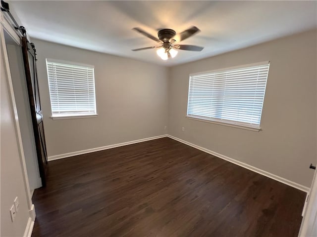 empty room with dark hardwood / wood-style flooring, a barn door, and ceiling fan