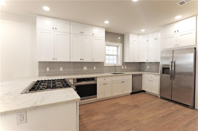 kitchen with light hardwood / wood-style floors, appliances with stainless steel finishes, sink, and decorative backsplash