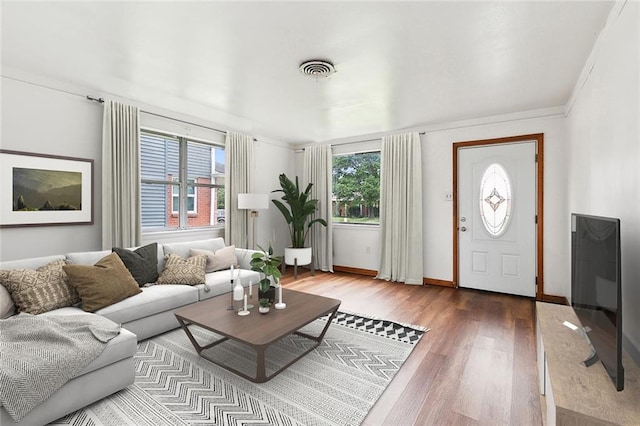 living area with a wealth of natural light, visible vents, baseboards, and wood finished floors