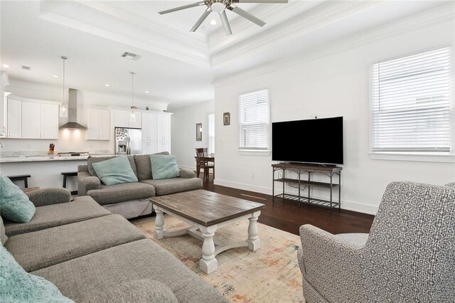 living room with a raised ceiling, ceiling fan, dark wood-type flooring, and a healthy amount of sunlight