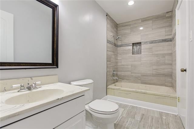 full bathroom featuring wood-type flooring, vanity, tiled shower / bath combo, and toilet