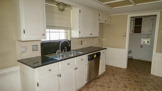 kitchen featuring tasteful backsplash, dark countertops, stainless steel dishwasher, white cabinetry, and a sink