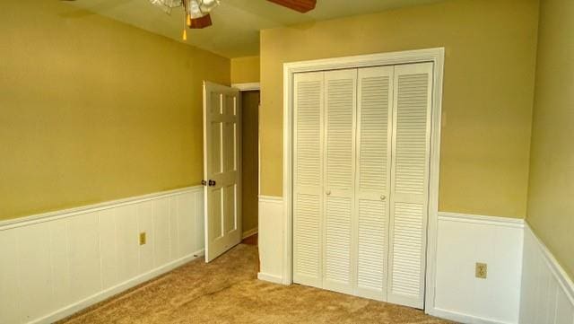 unfurnished bedroom with carpet floors, a ceiling fan, a closet, and wainscoting