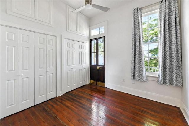 unfurnished bedroom with ceiling fan, two closets, and dark hardwood / wood-style floors