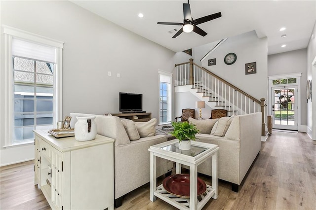 living room with a high ceiling, ceiling fan, and light wood-type flooring