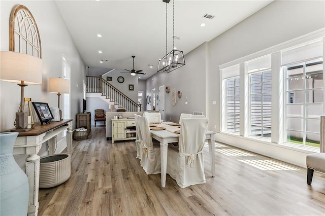 dining area with light hardwood / wood-style floors, ceiling fan with notable chandelier, and a towering ceiling