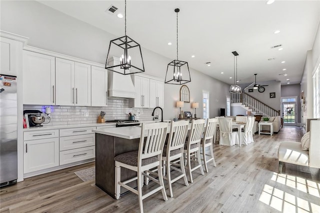 kitchen with decorative backsplash, a kitchen island with sink, custom exhaust hood, light hardwood / wood-style floors, and appliances with stainless steel finishes