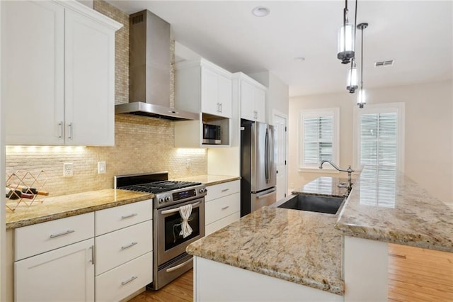 kitchen with wall chimney exhaust hood, stainless steel appliances, sink, pendant lighting, and a center island with sink