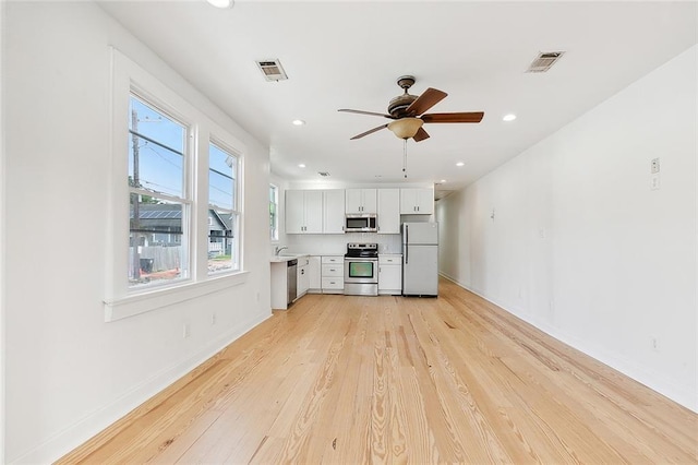 unfurnished living room featuring sink, plenty of natural light, ceiling fan, and light wood-type flooring