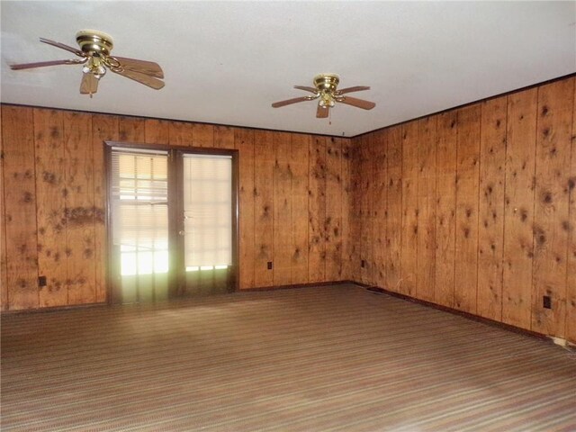 spare room featuring wooden walls, ceiling fan, and carpet flooring