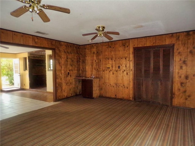 empty room with ceiling fan, wood walls, and tile patterned floors