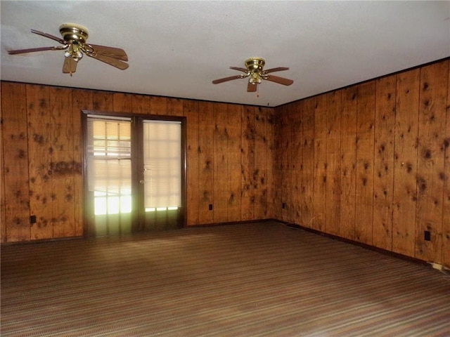 carpeted empty room with ceiling fan and wood walls