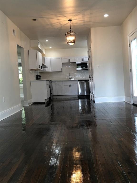 kitchen with appliances with stainless steel finishes, backsplash, white cabinetry, sink, and dark hardwood / wood-style flooring