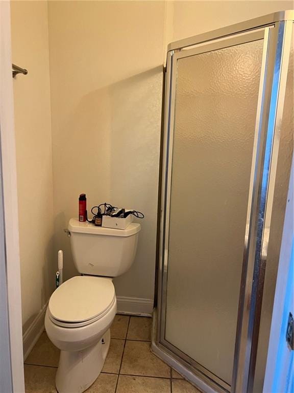 bathroom featuring toilet, a shower with door, and tile patterned floors