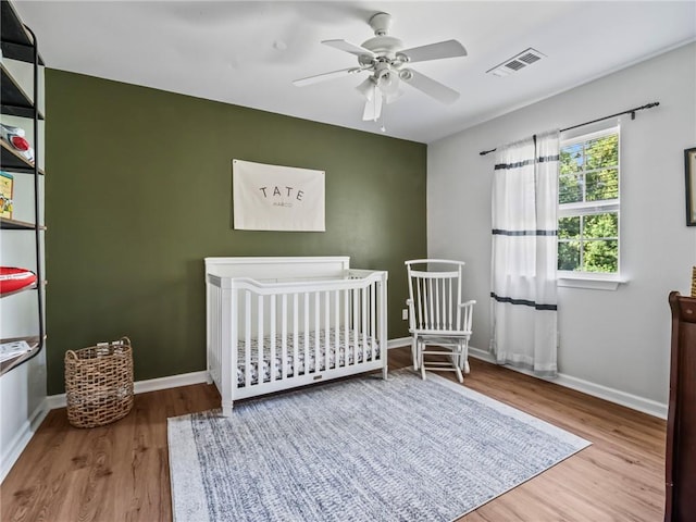 bedroom with ceiling fan, light hardwood / wood-style flooring, and a nursery area