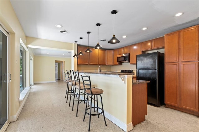 kitchen with a kitchen breakfast bar, pendant lighting, dark stone countertops, and black fridge