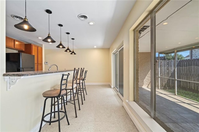 kitchen featuring a wealth of natural light, black refrigerator, pendant lighting, and a kitchen breakfast bar