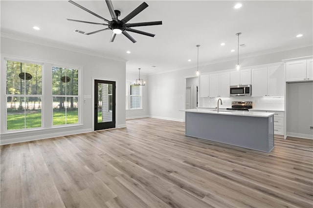 kitchen featuring appliances with stainless steel finishes, white cabinetry, crown molding, light wood-type flooring, and a kitchen island with sink