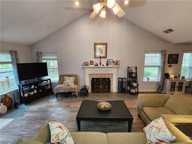 living room with tile patterned flooring, a tiled fireplace, ceiling fan, and high vaulted ceiling