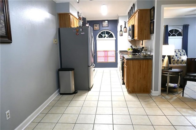 kitchen with brown cabinets, crown molding, light tile patterned floors, stainless steel appliances, and dark countertops