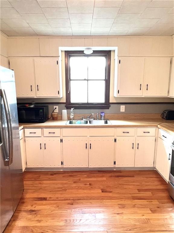 kitchen with appliances with stainless steel finishes, light hardwood / wood-style floors, white cabinets, and sink