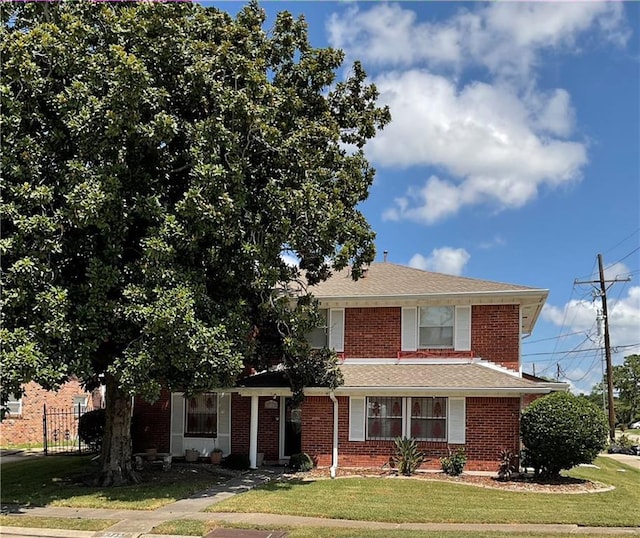 traditional-style home with brick siding, roof with shingles, a front yard, and fence