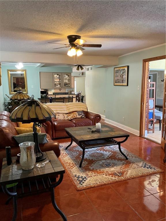 tiled living room featuring a textured ceiling, ceiling fan, and ornamental molding