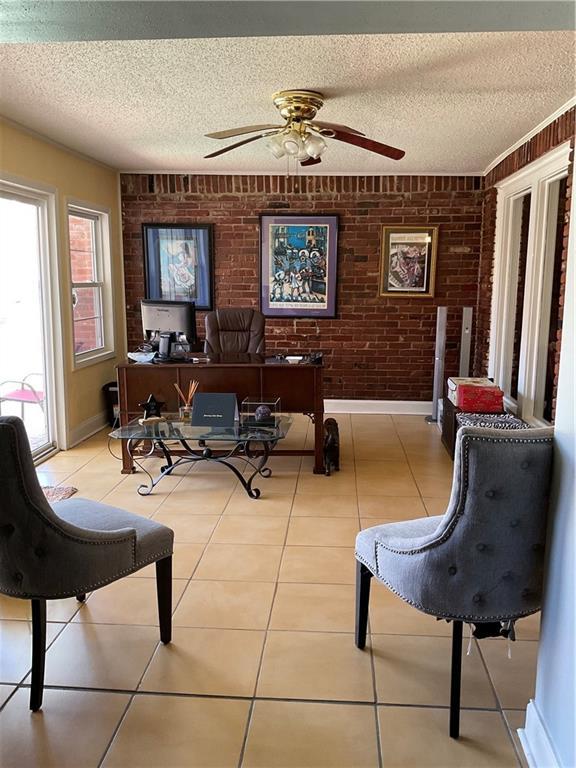 office space featuring ceiling fan, light tile patterned flooring, and brick wall