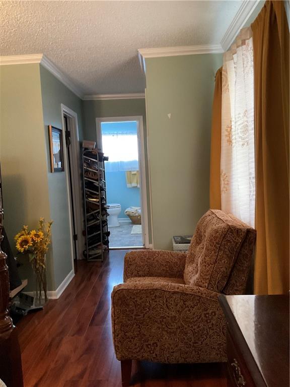 living area featuring a textured ceiling, dark wood-type flooring, baseboards, and crown molding