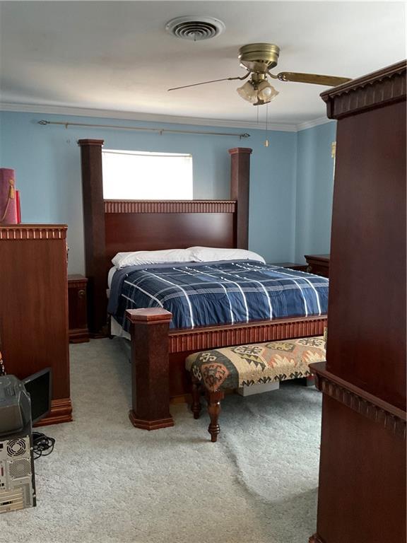 bedroom with ceiling fan, ornamental molding, visible vents, and light colored carpet