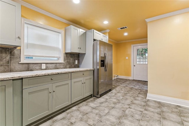 kitchen featuring decorative backsplash, stainless steel refrigerator with ice dispenser, crown molding, light stone countertops, and light tile patterned flooring