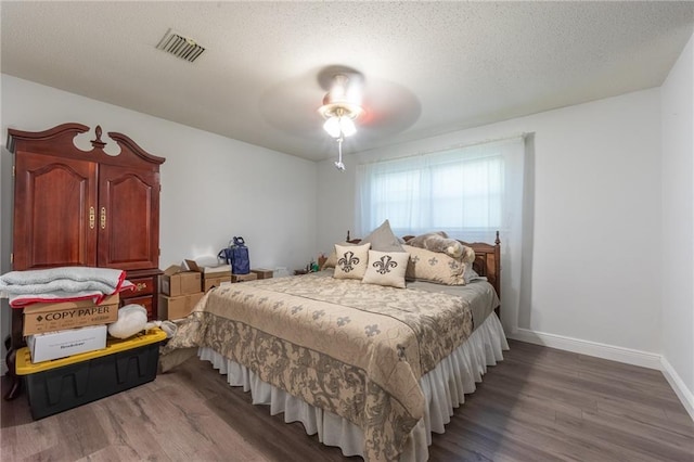 bedroom with visible vents, a textured ceiling, baseboards, and wood finished floors