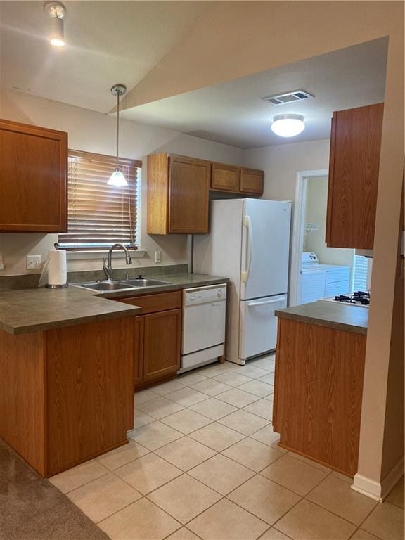 kitchen with white appliances, a sink, brown cabinetry, dark countertops, and decorative light fixtures