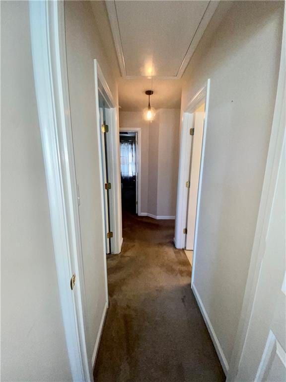 hall with dark carpet, attic access, and baseboards