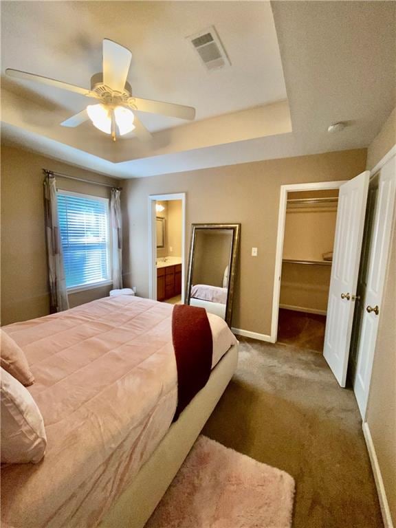 carpeted bedroom with a tray ceiling, a closet, ceiling fan, and ensuite bathroom