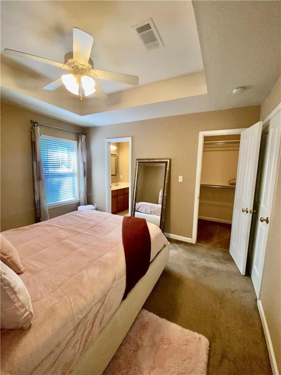 bedroom with baseboards, visible vents, a raised ceiling, ceiling fan, and carpet floors