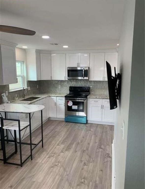 kitchen with appliances with stainless steel finishes, light hardwood / wood-style floors, decorative backsplash, sink, and white cabinets