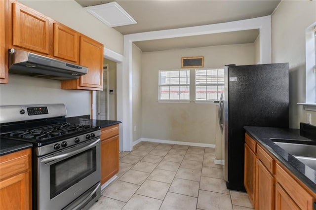 2546 Elder St, New Orleans, LA 70122 - kitchen featuring brown cabinets, under cabinet range hood, stainless steel appliances, light tile patterned floors, and baseboards
