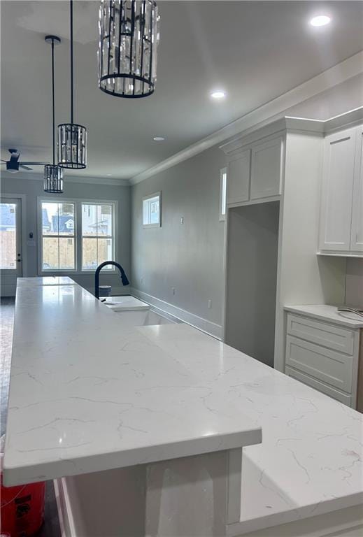 kitchen featuring pendant lighting, light stone counters, crown molding, and white cabinetry