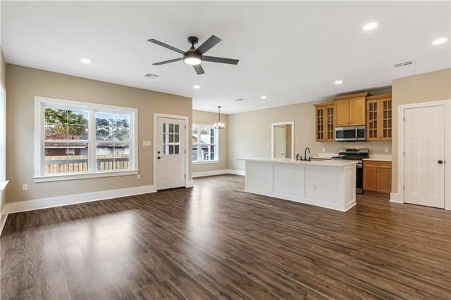 kitchen featuring plenty of natural light, range, an island with sink, dark wood-type flooring, and hanging light fixtures