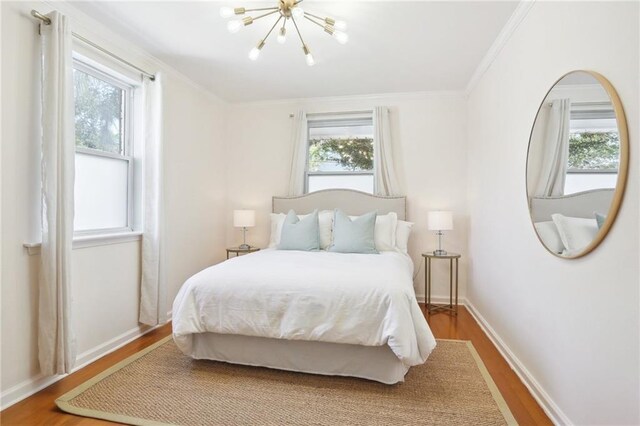 bedroom featuring multiple windows, hardwood / wood-style floors, an inviting chandelier, and ornamental molding