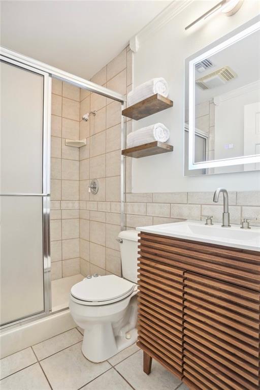 bathroom featuring vanity, tile patterned floors, toilet, tile walls, and an enclosed shower