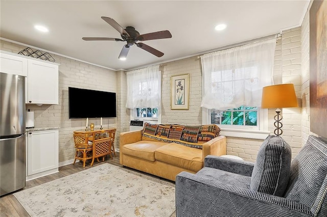 living room with light hardwood / wood-style flooring, ceiling fan, and brick wall