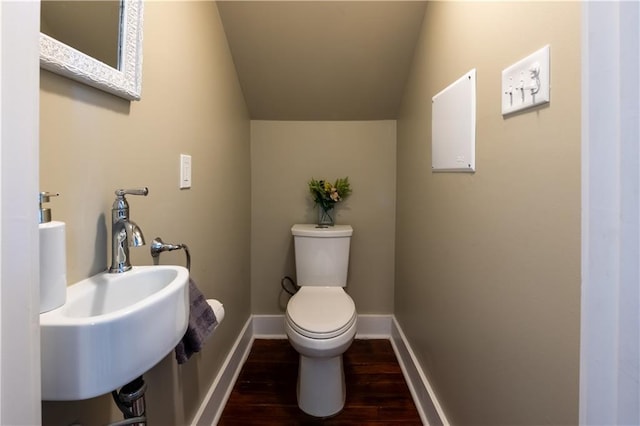 bathroom with wood-type flooring, vaulted ceiling, toilet, and sink