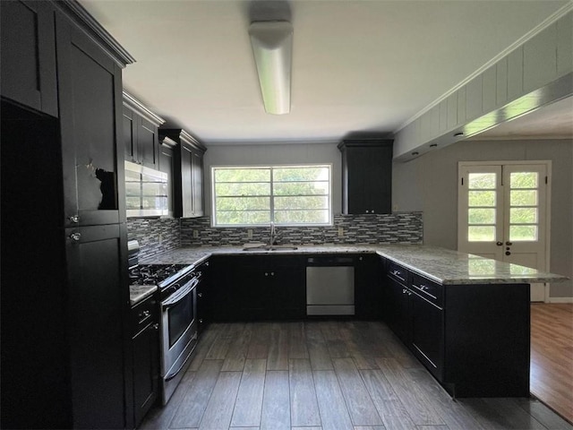 kitchen with appliances with stainless steel finishes, dark cabinets, a peninsula, and light stone countertops