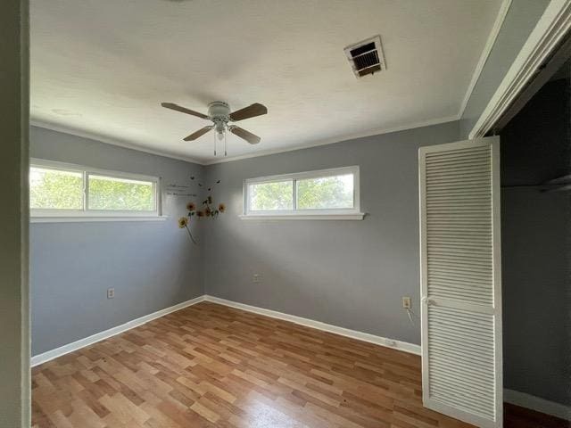 unfurnished bedroom featuring wood finished floors, visible vents, baseboards, ornamental molding, and a closet