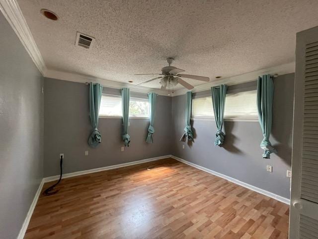 unfurnished room featuring crown molding, visible vents, a textured ceiling, wood finished floors, and baseboards